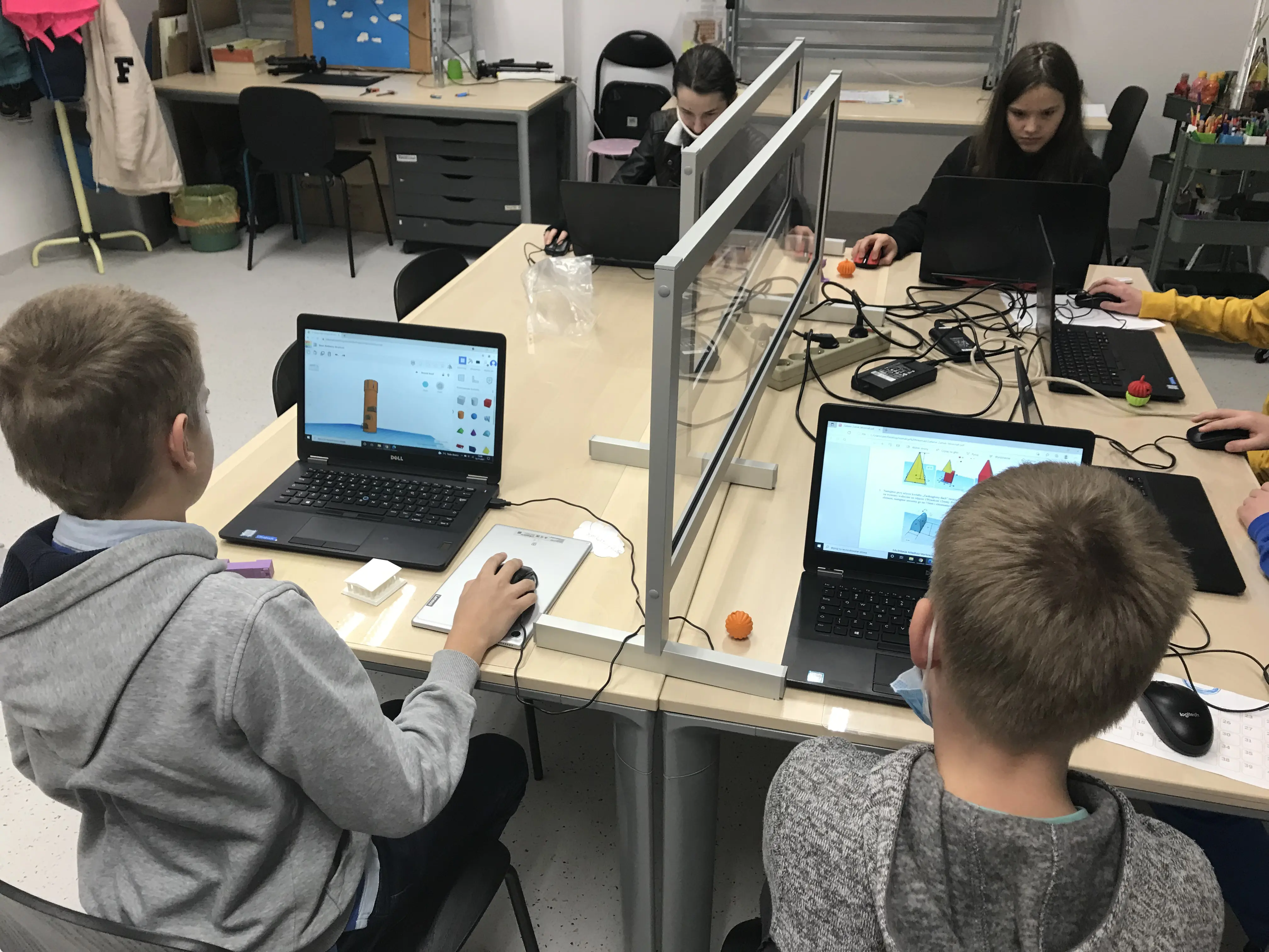 Uczniowie przy laptopach z wydrukowanymi modelami na biurkach