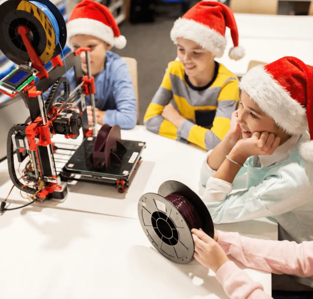 Dzieci w mikołajkowych czapkach obserwują pracującą drukarkę 3D